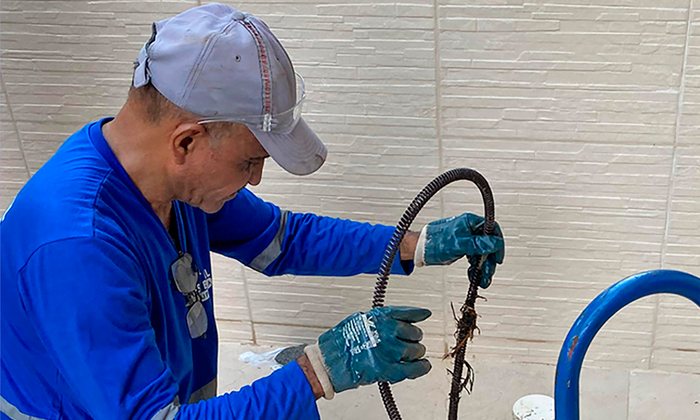 Técnico da Mendes Brasil Desentupidora desentupindo ralo com máquina rotativa